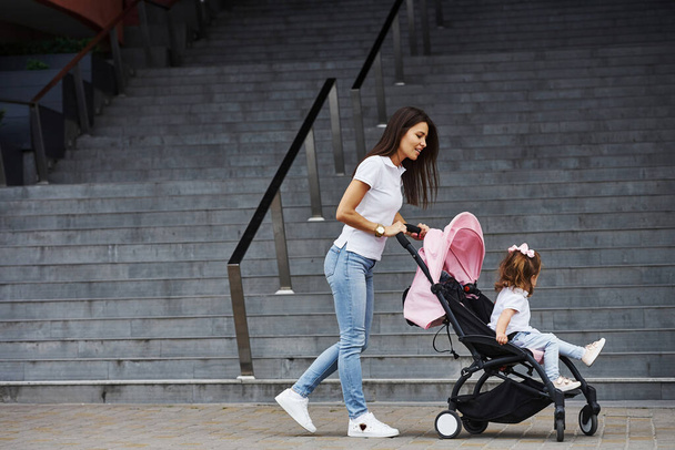 Pretty young mother and her little daughter in pink pram have walk in the city. - Φωτογραφία, εικόνα