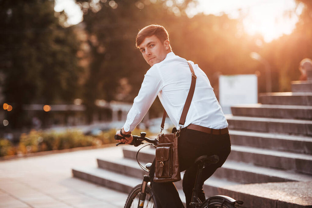 Looking behind. Businessman in formal clothes with black bicycle is in the city. - Photo, image