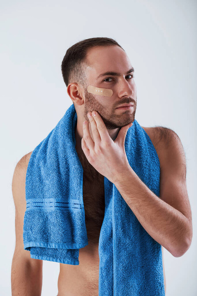 Caucasian ethnicity. Man with blue towel stands against white background in the studio. - Фото, изображение