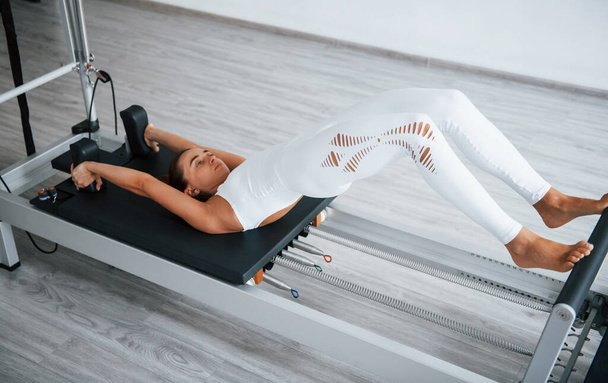 Working hard. Confident young sporty woman with slim body type in the healthy center doing exercises by using special equipment. - Zdjęcie, obraz