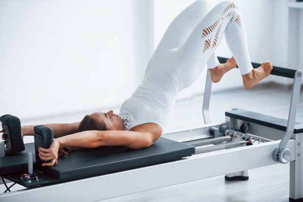 Good for the spine. Confident young sporty woman with slim body type in the healthy center doing exercises by using special equipment. - Zdjęcie, obraz