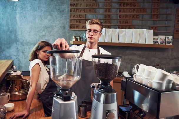Behind the coffee machine. Two young workers indoors. Conception of business and service. - 写真・画像
