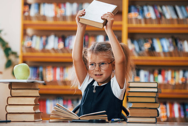 Cute little girl with pigtails is in the library. Apple on the books. - Foto, Bild