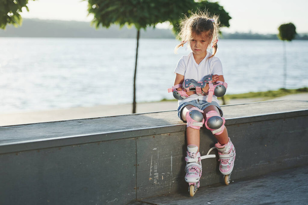 Cute little girl with roller skates outdoors sits on the ramp for extreme sports. - Foto, Bild