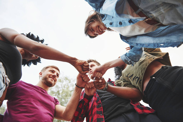Giving bro fist. Multi ethnic group of people have party outdoors. View from down. - 写真・画像