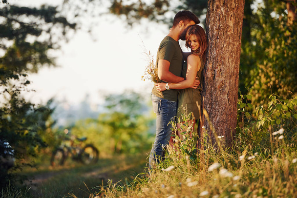 Leaning on the tree. Beautiful young couple have a good time in the forest at daytime. - Fotó, kép
