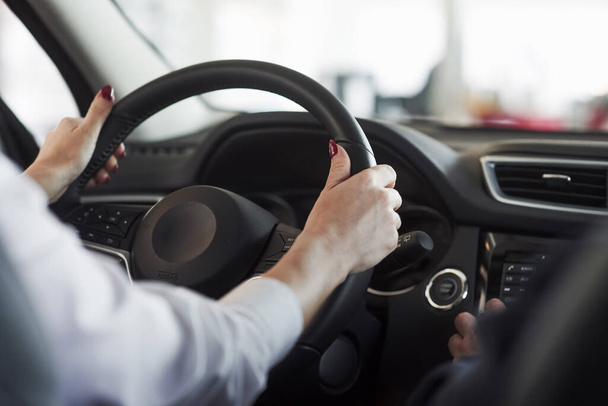 Hands on steering wheel. Woman in official clothes trying her new car in automobile salon. - Foto, afbeelding