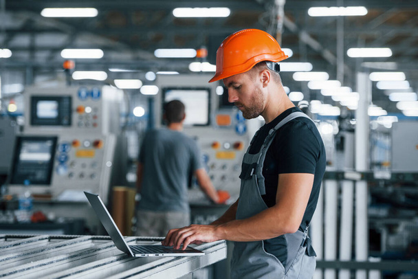 Modern laptop. Typing on keyboard. Industrial worker indoors in factory. Young technician with orange hard hat. - Photo, image