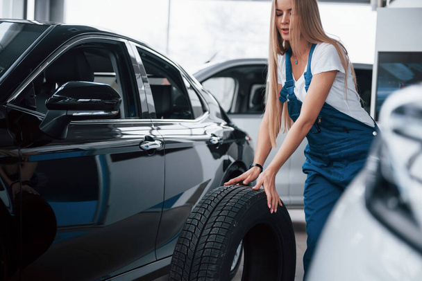 Rolling new wheel. Woman walks to the car. Conception of repair. - Foto, afbeelding