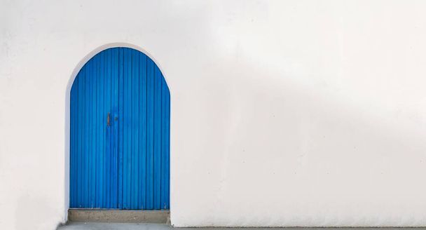 Μπλε ξύλινη vintage κλειστή πόρτα με καμάρα σε άδειο ασβεστωμένο φόντο τοίχου. Κυκλάδες Ελληνική νησιώτικη αρχιτεκτονική, λευκό αντίγραφο space card template διαφήμιση. - Φωτογραφία, εικόνα