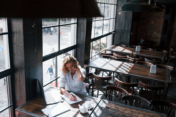 Aerial view. Businesswoman with curly blonde hair indoors in cafe at daytime. - Zdjęcie, obraz