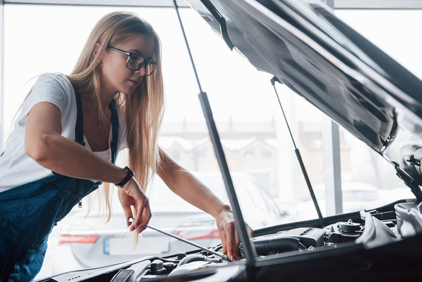Other automobile through the window. On the lovely job. Car addicted woman repairs black automobile indoors. - Photo, image