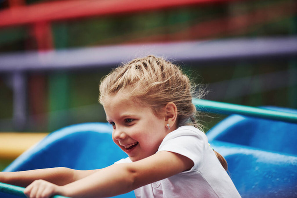 Portrait of happy female kid have fun on a roller coaster in the park at daytime. - Photo, Image