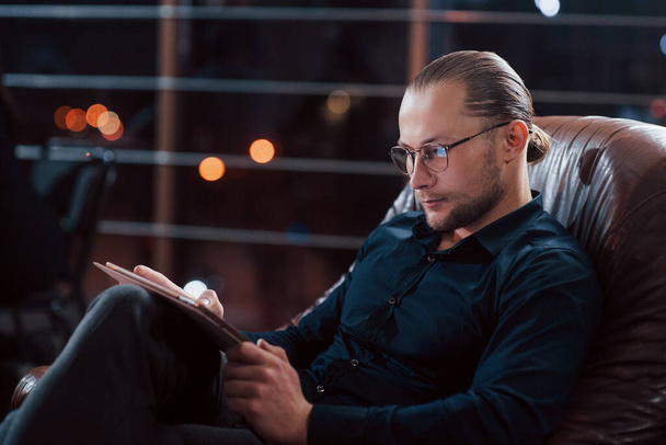 Reading the information. Stylish businessman in eyewear works alone in the office at nightime. - Fotoğraf, Görsel