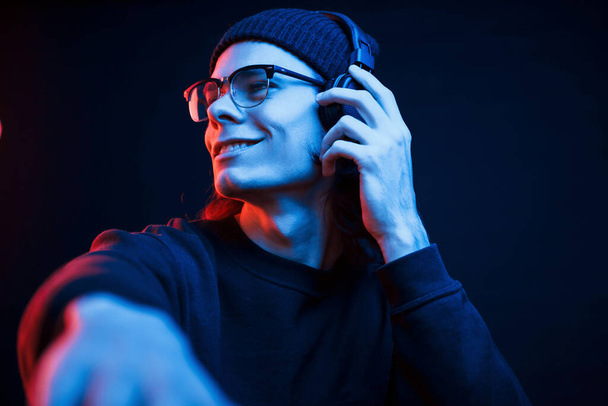 DJ on his job. Studio shot in dark studio with neon light. Portrait of serious man. - Фото, изображение
