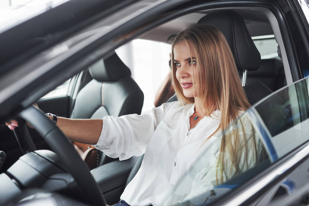 Let's ride. Beautiful blonde girl sitting in the new car with modern black interior. - Photo, image