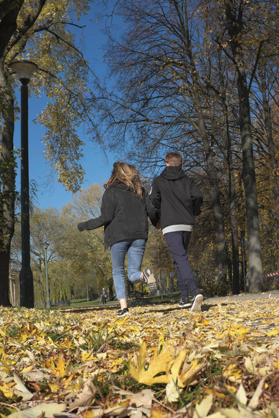 Autumn, a couple of young people are running in the city park ... - Fotoğraf, Görsel