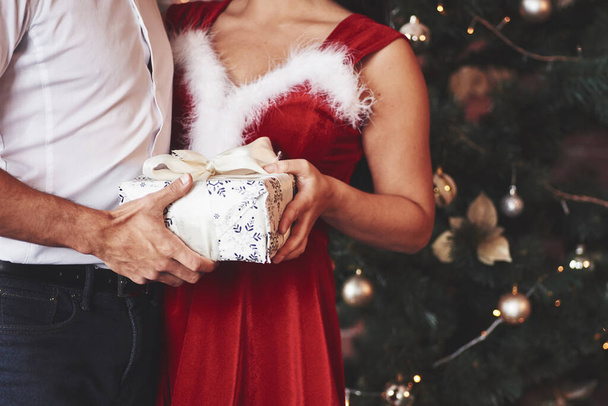 Vacaciones finalmente. Hermosa pareja celebrando Año Nuevo en la habitación decorada con árbol de Navidad detrás. - Foto, imagen