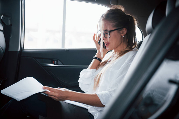 Work will not wait. Smart businesswoman sits at backseat of the luxury car with black interior. - Foto, Imagem