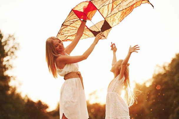 With hands up. Mother and daughter have fun with kite in the field. Beautiful nature. - 写真・画像