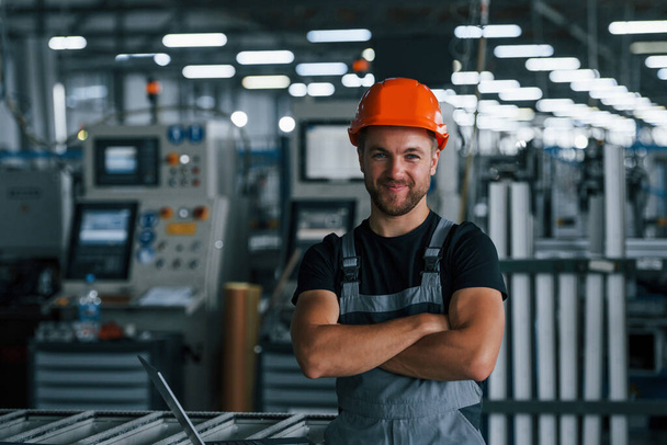 Portrait of industrial worker indoors in factory. Young technician with orange hard hat. - Zdjęcie, obraz