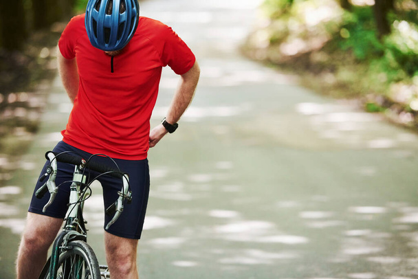 Preparing for a ride. Cyclist on a bike is on the asphalt road in the forest at sunny day. - Foto, imagen
