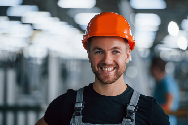 Smiling and happy employee. Portrait of industrial worker indoors in factory. Young technician with orange hard hat. - Photo, Image