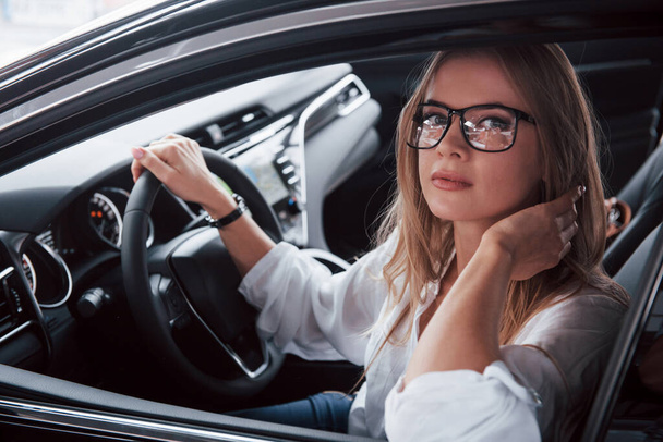 Muotialan nainen. Kaunis blondi tyttö istuu uudessa autossa, jossa on moderni musta sisustus. - Valokuva, kuva