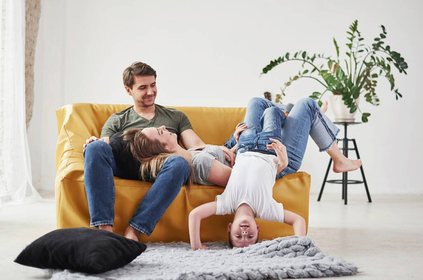 Child fools around. Happy family have fun on the yellow sofa in the living room of their new house. - 写真・画像