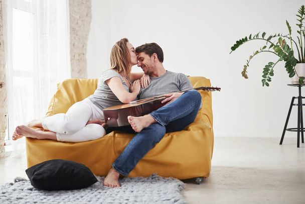 Wdzięczna dziewczyna daje buziaka. Szczęśliwa para relaksująca się na żółtej kanapie w salonie swojego nowego domu. - Zdjęcie, obraz