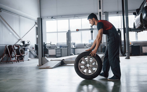 Spacious room. Mechanic holding a tire at the repair garage. Replacement of winter and summer tires. - Foto, Imagen