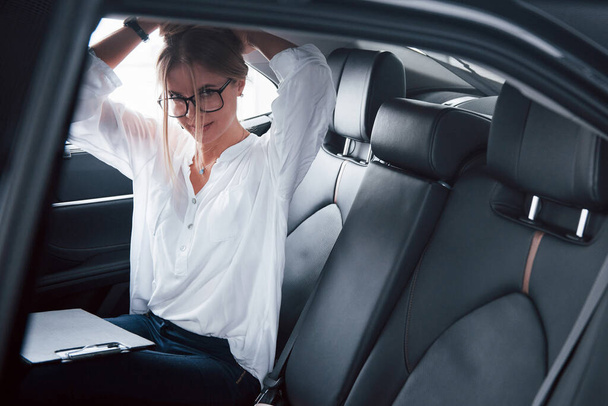 Upravuju vlasy. Chytrá podnikatelka sedí na zadním sedadle luxusního vozu s černým interiérem. - Fotografie, Obrázek