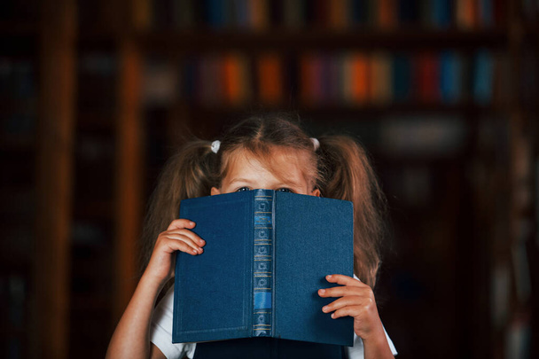 Having fun. Cute little girl stands in the library full of books. Conception of education. - Foto, imagen