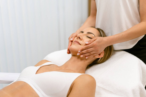 Middelbare leeftijd vrouw met een hoofd massage in een schoonheidssalon. - Foto, afbeelding