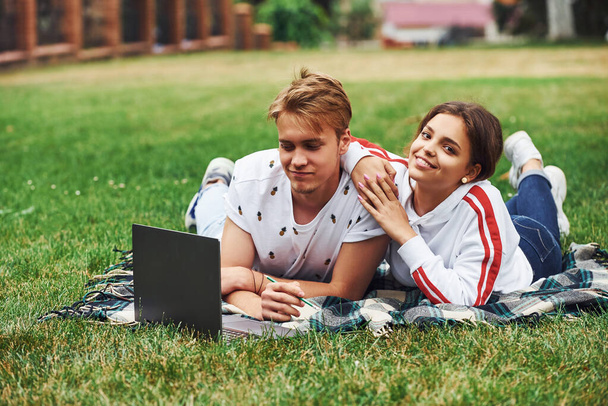 Young couple sits on green grass on the field with their laptop. - Foto, Bild