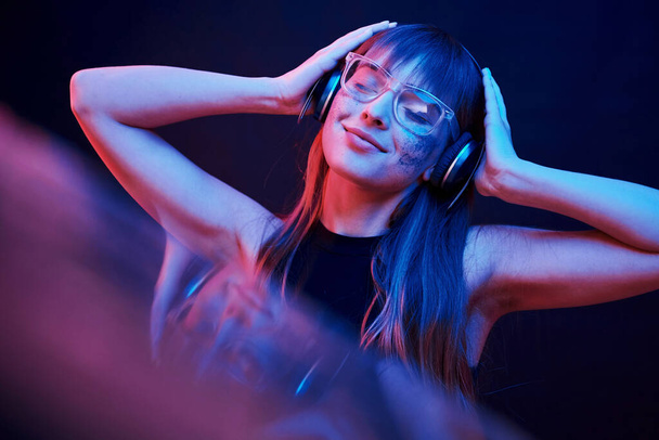 Stylish glasses. Studio shot in dark studio with neon light. Portrait of young girl. - Фото, изображение