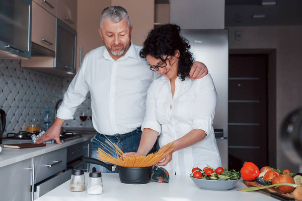 簡単だ。台所で野菜を使った料理を作る白いシャツを着た男と妻. - 写真・画像