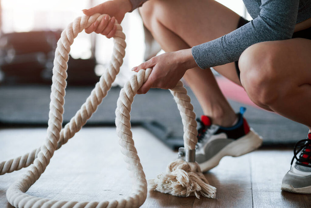 Special white rope in hands. Sportive young woman have fitness day in the gym at morning time. - Фото, зображення