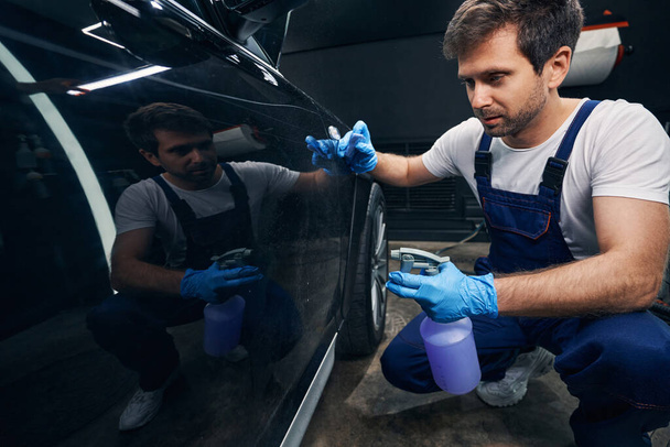 Auto repair shop worker spraying car with degreasing liquid - Foto, afbeelding