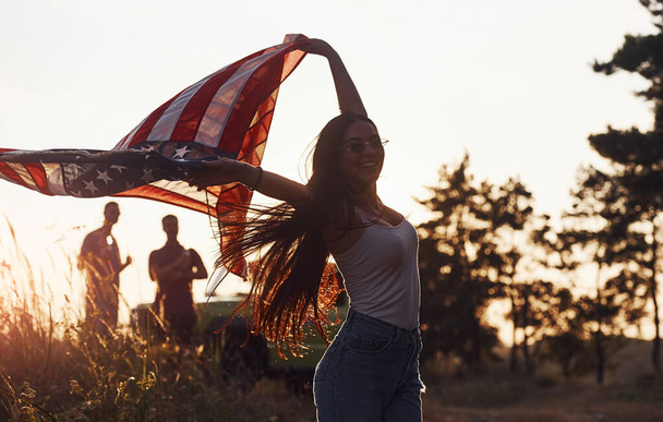 Feels freedom. Friends have nice weekend outdoors near theirs green car with USA flag. - Фото, зображення