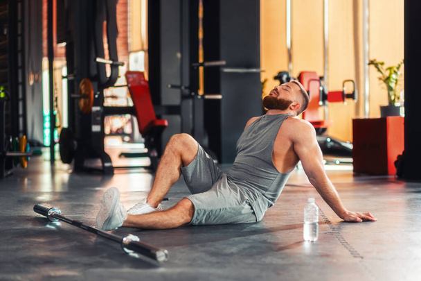 運動後、床の上で筋肉運動選手の男性がリラックスします。ベルは足の近くにある。フィットネスとボディービルの概念. - 写真・画像