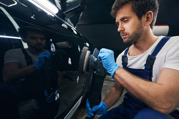 Caucasian repairman polishing body of car in automotive service - Foto, Imagen