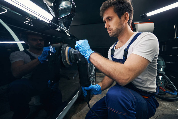 Male car repairman polishing autobody surface with instrument - Foto, Imagen