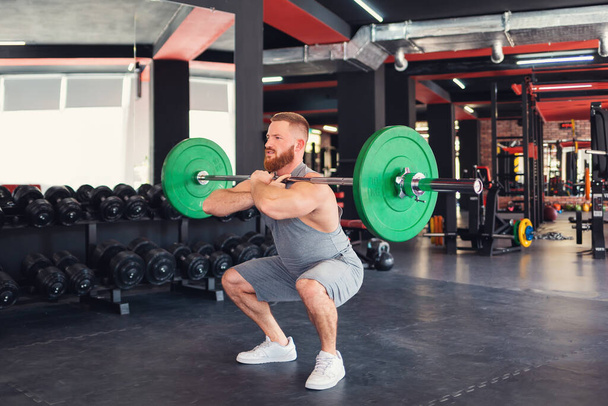 Barbell squats. A bearded athletic man trains in the gym, lifting a barbell. Keeping fit with cross training. - Foto, Imagen