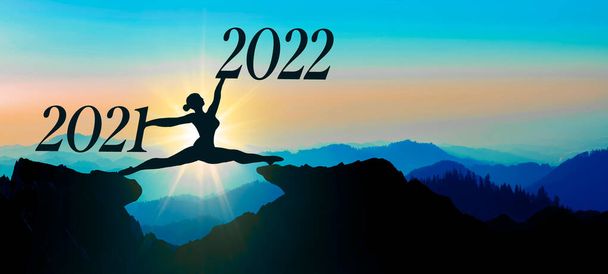 С Новым 2022 годом фоновая баннерная панорама - Молодая балерина совершает сплит-прыжок между 2021 и 2022 годами под солнцем и через зазор холма горы ландшафтного силуэта в красочном вечернем небе - Фото, изображение