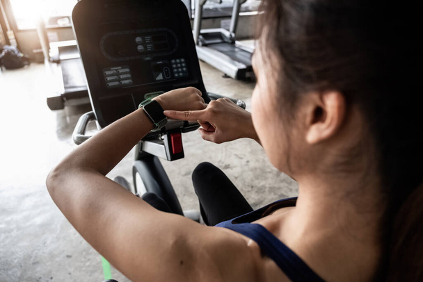 Jonge vrouw workout in fitnessruimte gezonde levensstijl, vrouw is met behulp van slimme horloge tijdens haar training met spinnen of cyclo - Foto, afbeelding
