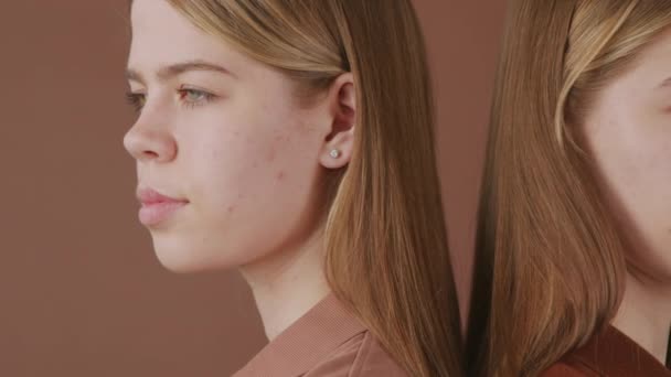 Panning close up shot of identical twin sisters standing back to back against brown background - Footage, Video