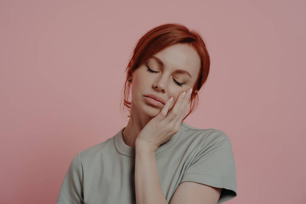 Unelias väsynyt punatukkainen nainen torkkuu käsillä, nukahtaa, eristetty vaaleanpunainen tausta - Valokuva, kuva