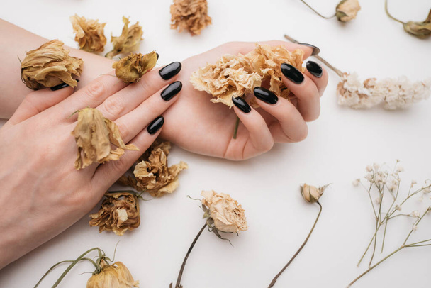 Black manicure on female hands. Hands are decorated with dried flowers. - Foto, afbeelding