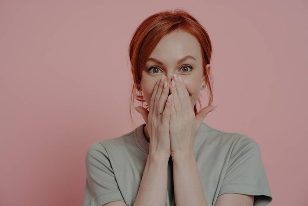 Young pretty ginger woman covering mouth with both hands, being in shock and disbelief - Photo, Image